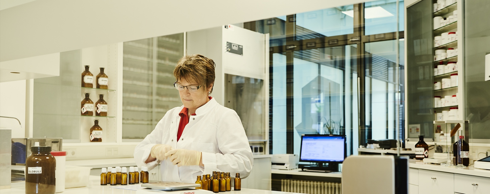 Eine Mitarbeiterin der Paracelsus-Apotheke im Laborkittel arbeitet mit braunen Apothekerfläschchen