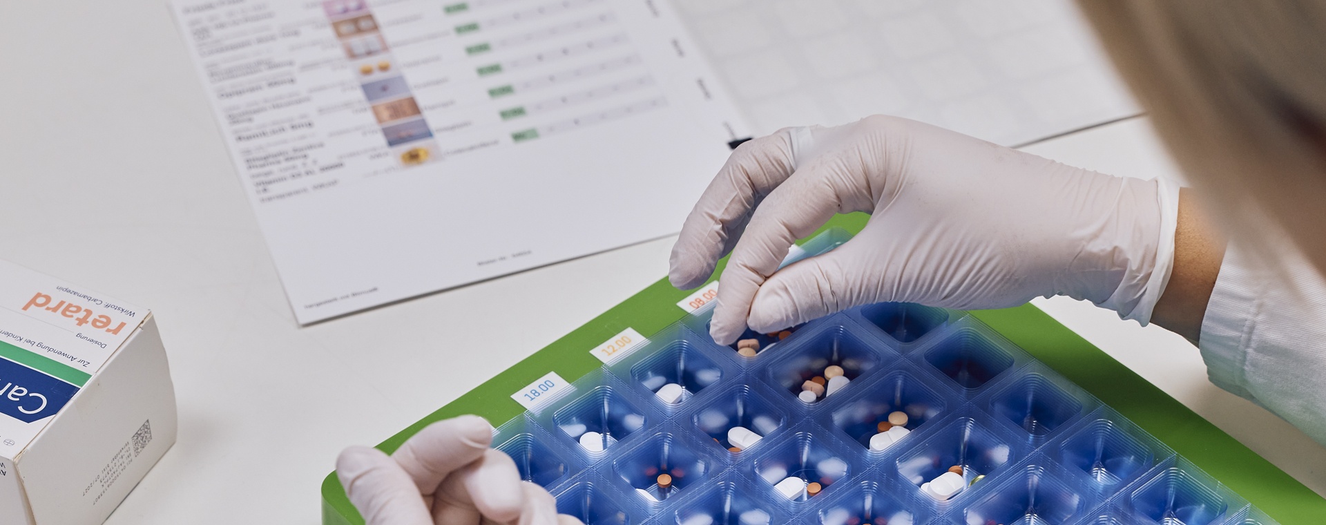 Eine Person mit weißen Handschuhen sortiert die Pillen in eine blaue Verpackung